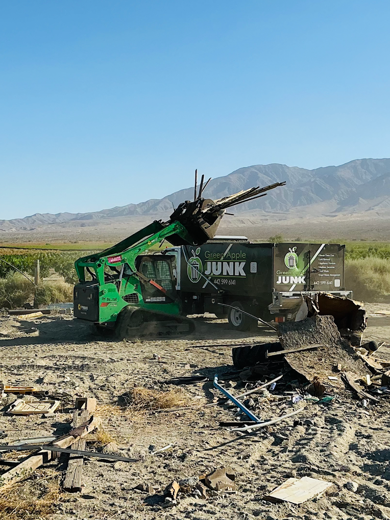 Green Apple grapple loader clearing construction debris with Coachella Valley mountains